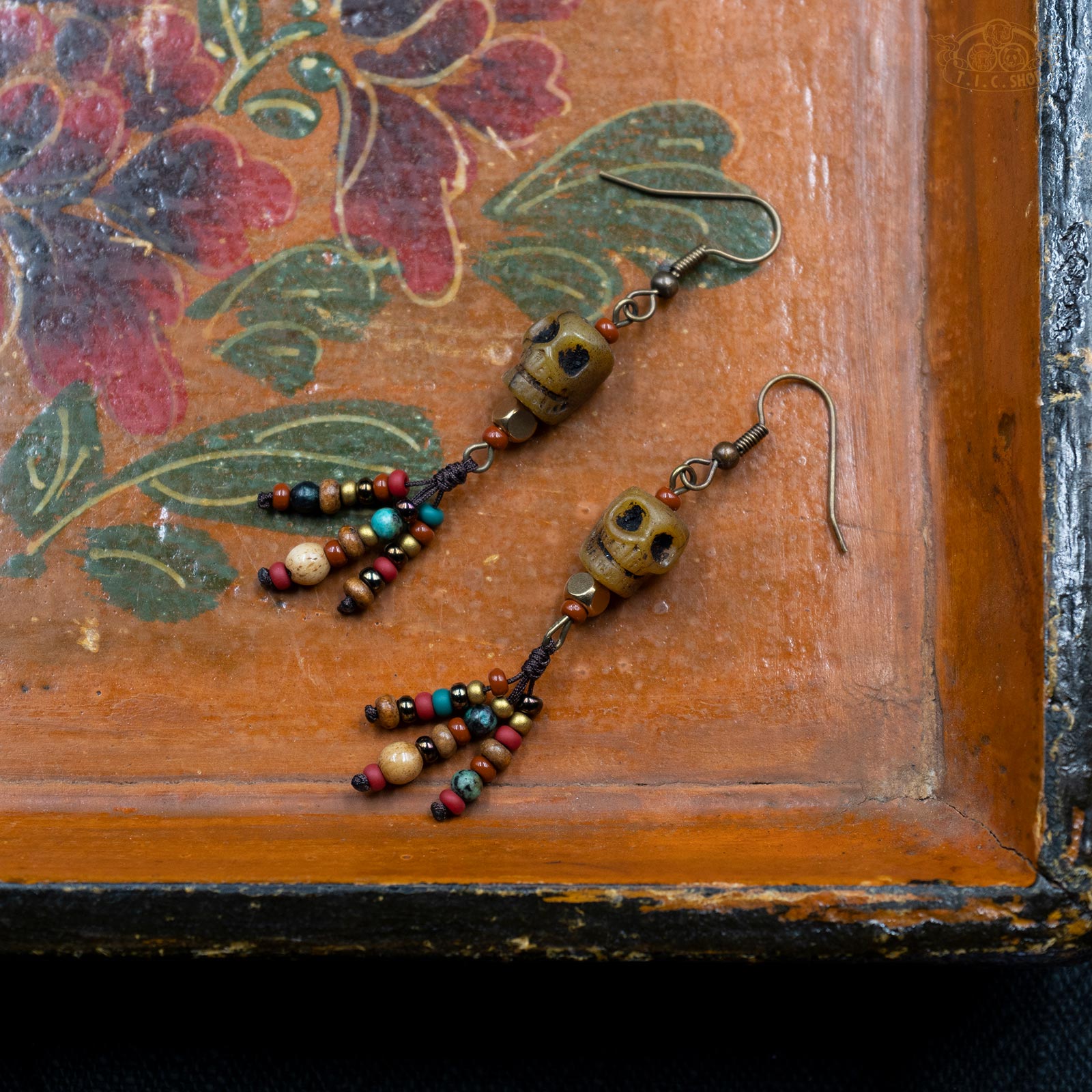 Each piece features a hand-carved yak bone skull, complemented by a colorful beaded tassel that creates a striking yet harmonious contrast. The bronze-finished ear hooks add a subtle vintage charm.