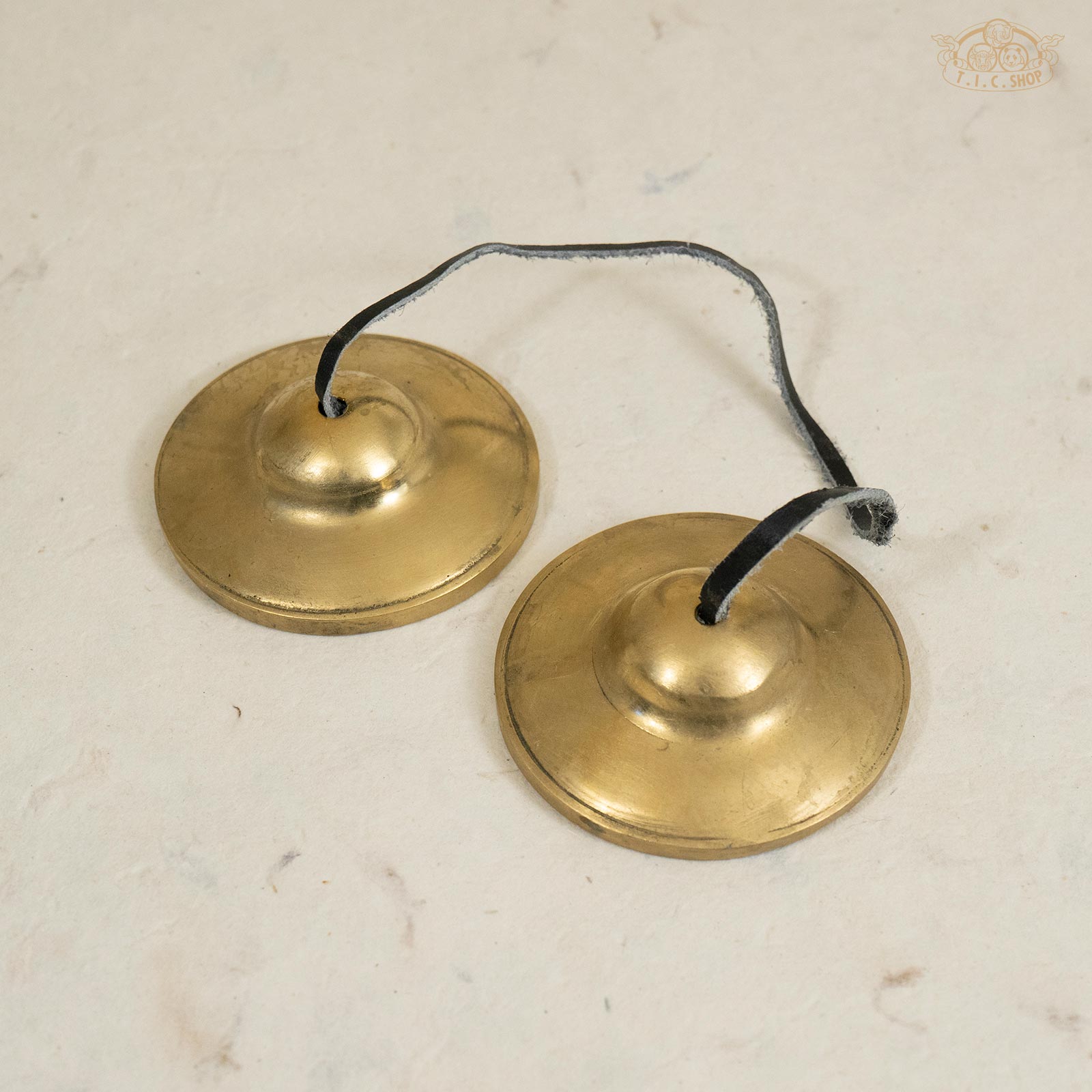 Front view of medium-sized plain Tibetan handmade brass Tingsha bells, joined by a leather strap.