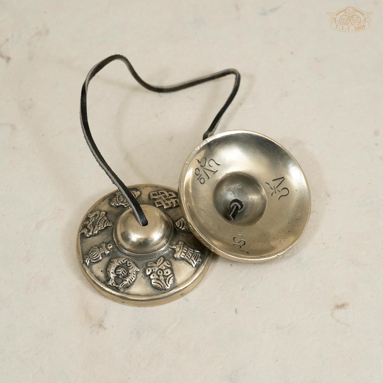 Back view of Tibetan brass Tingsha bells showing engraved 8 auspicious symbols and polished brass surface.