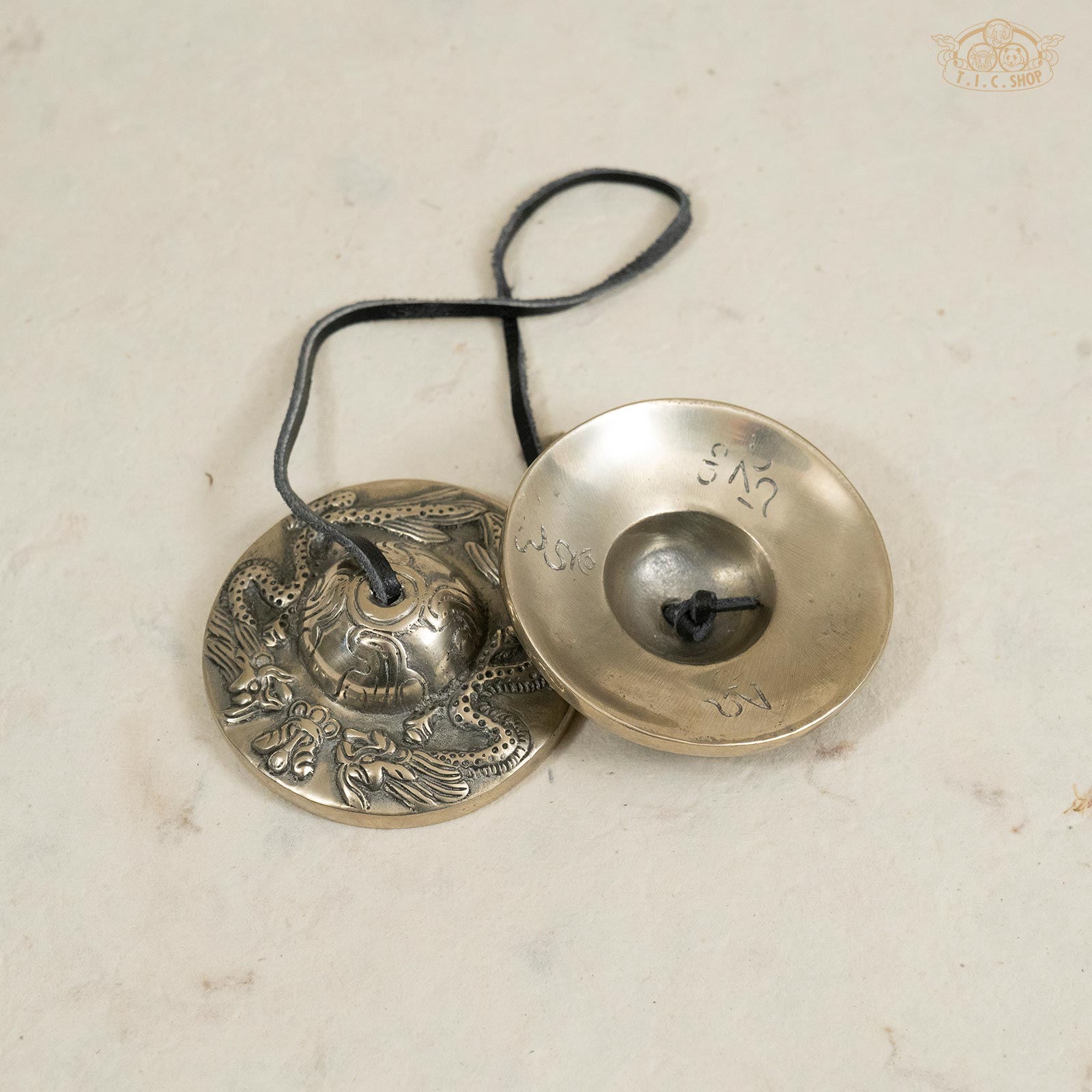 Back view of Tibetan brass Tingsha bells showing engraved dragon patterns and smooth metallic finish.