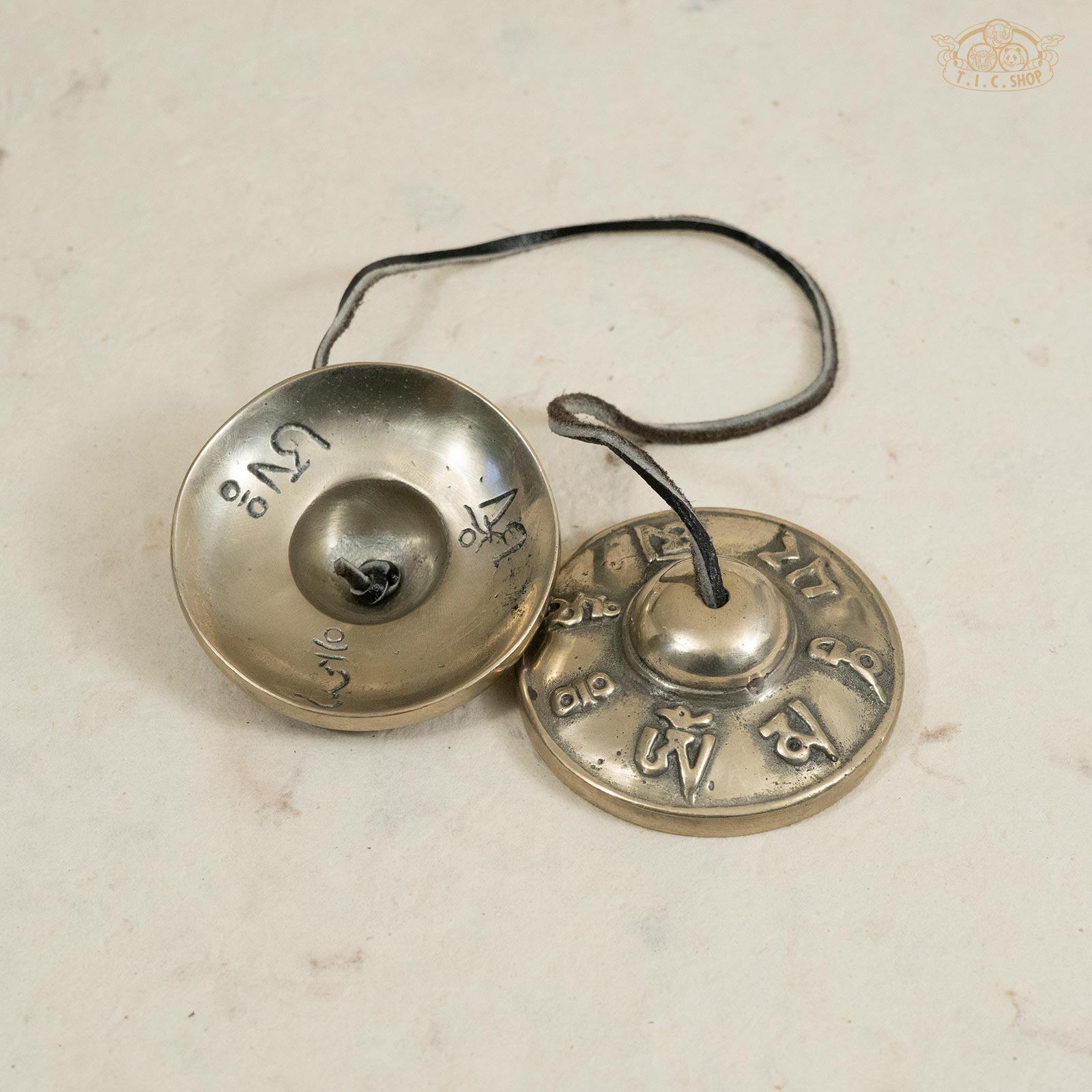 Back view of Tibetan brass Tingsha bells showing the engraved Om Mani Padme Hum mantra and polished surface.
