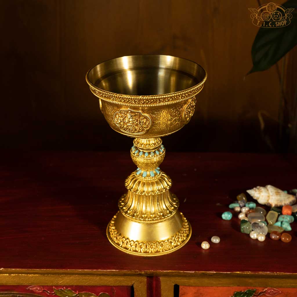 Side view of brass butter lamp showing detailed relief carvings and smooth polished surface.