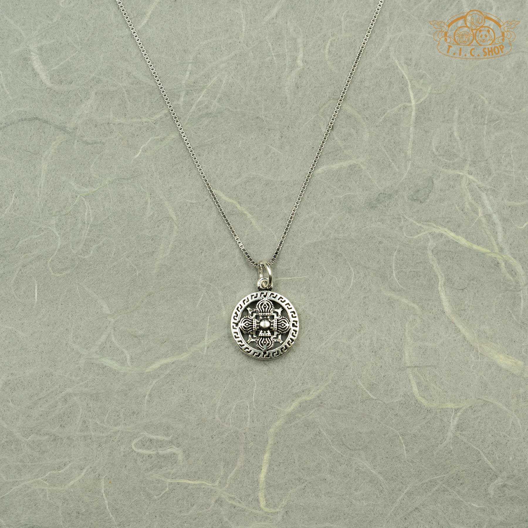 Direct front view of the circular silver Vishvavajra pendant featuring the traditional meander border design.