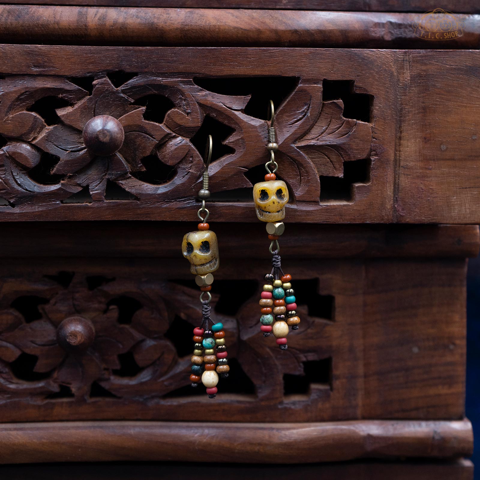 A pair of handmade earrings featuring carved yak bone skulls with bead decorations, displayed in a wooden box.