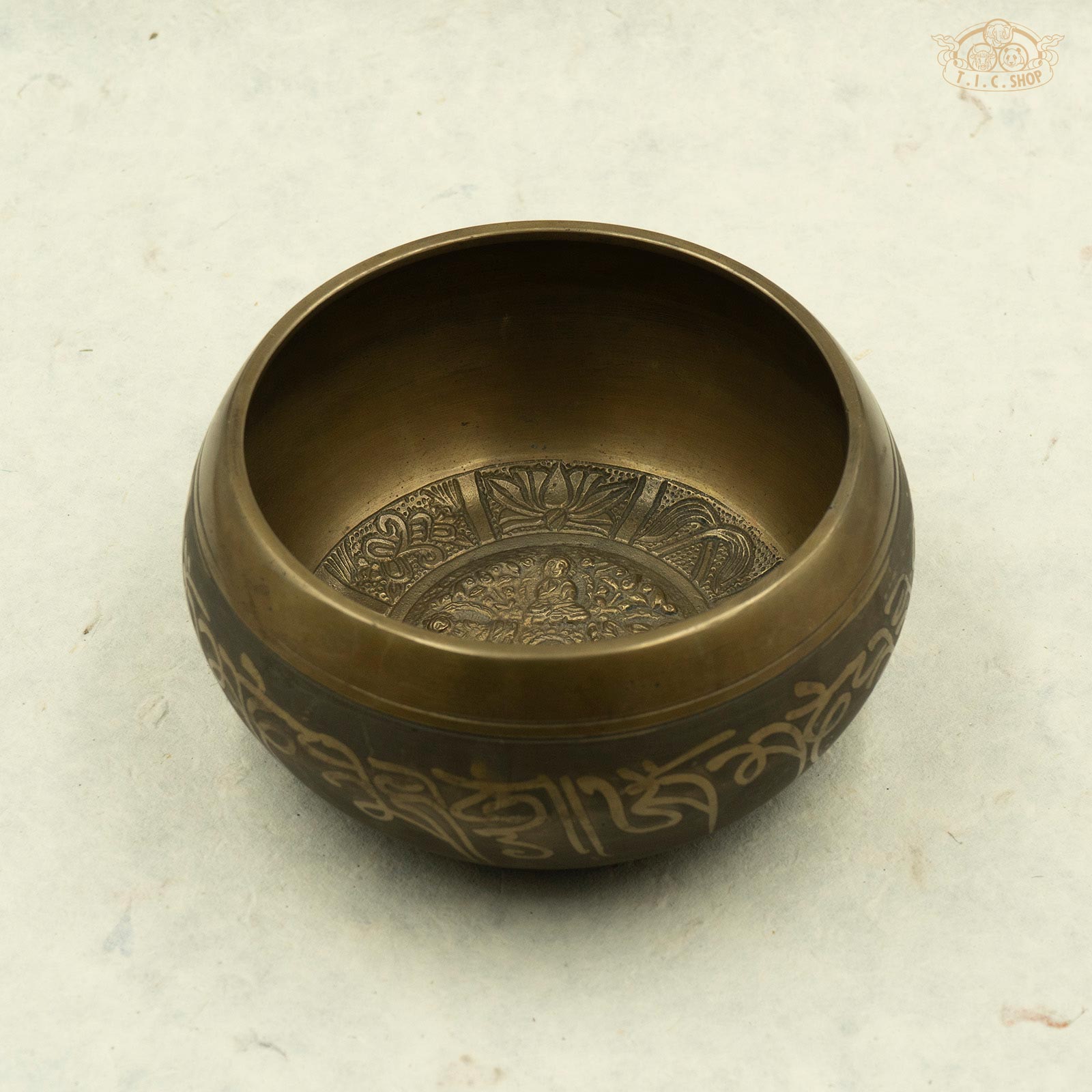 A brass singing bowl with an image of five buddhas around the rim, handcrafted in Nepal.