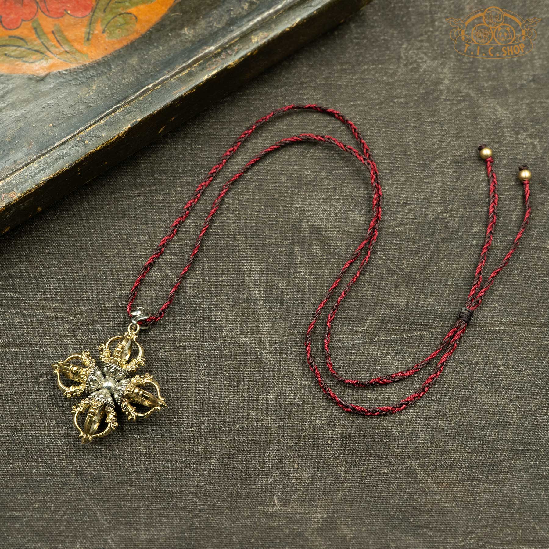 Sculpted double vajra pendant displayed with hand-woven red and brown rope necklace