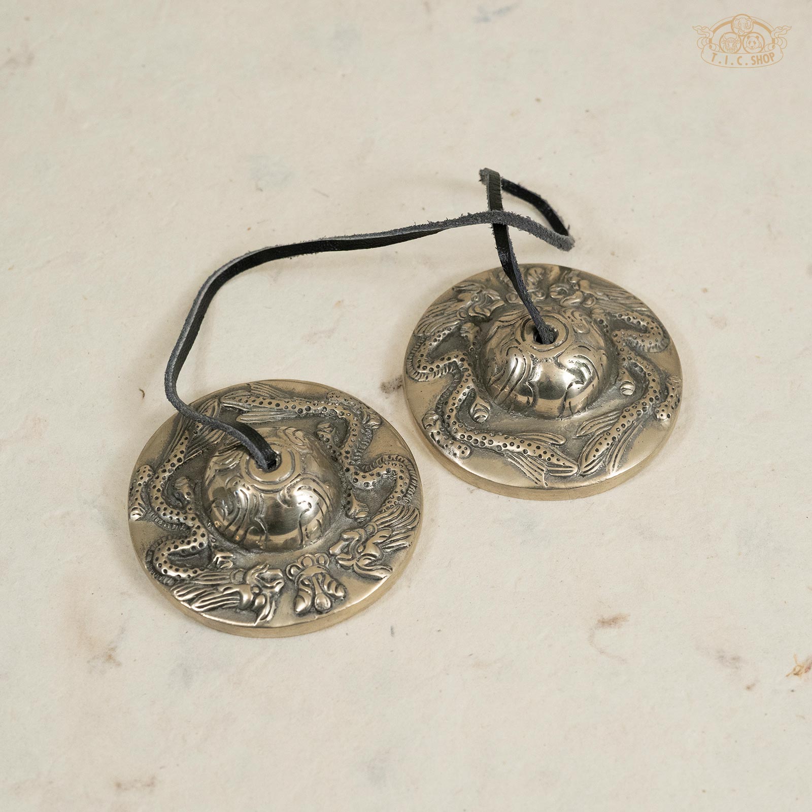 Front view of Tibetan handmade brass Tingsha bells with detailed dragon motifs and leather strap connection.