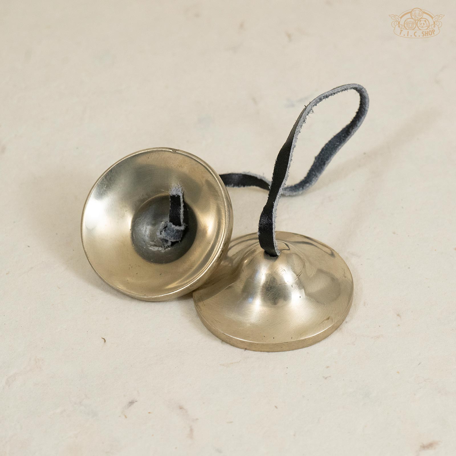Back view of Tibetan brass Tingsha bells displaying smooth metal finish and leather strap connection.
