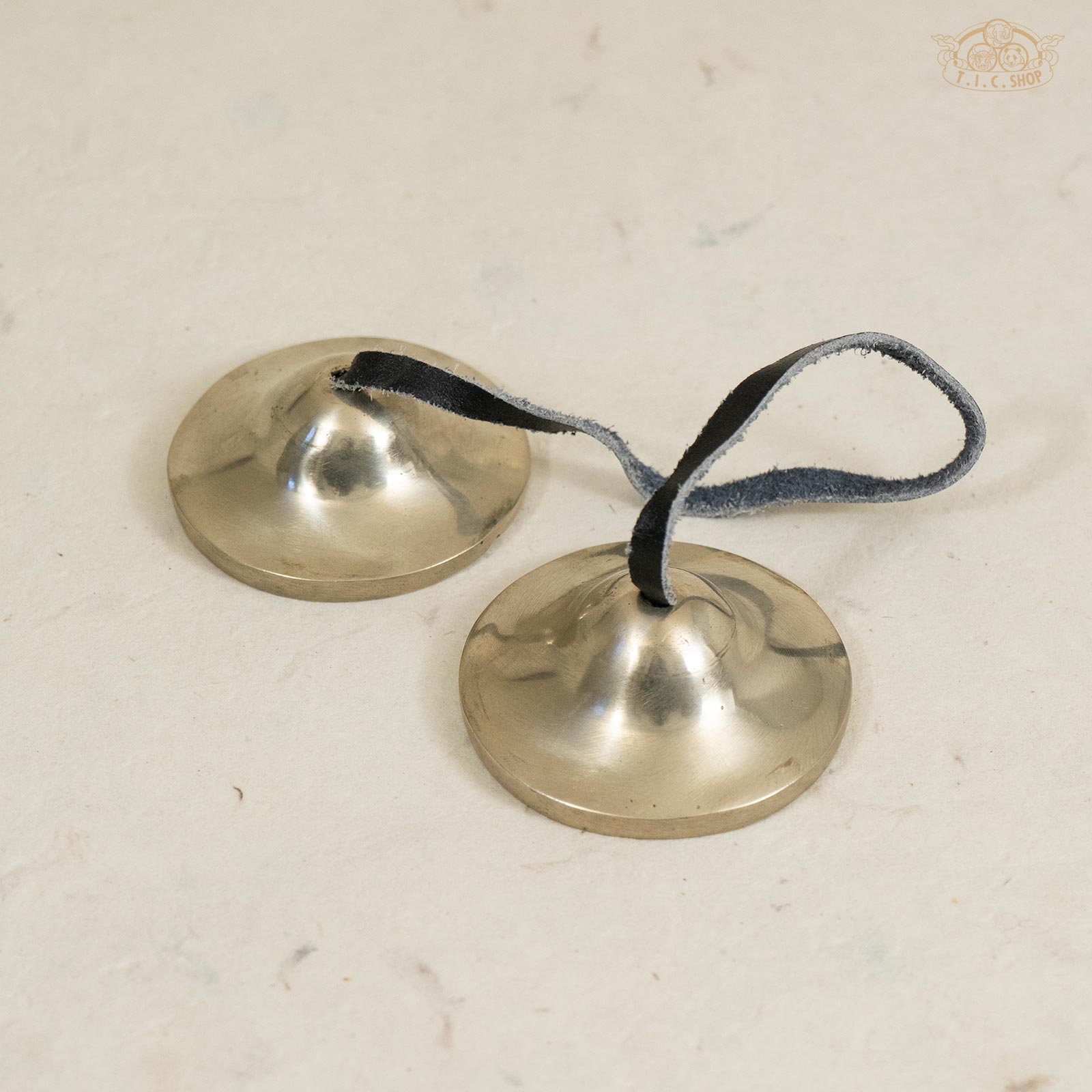 Front view of Tibetan handmade brass Tingsha bells connected by a leather strap, showing polished surface.