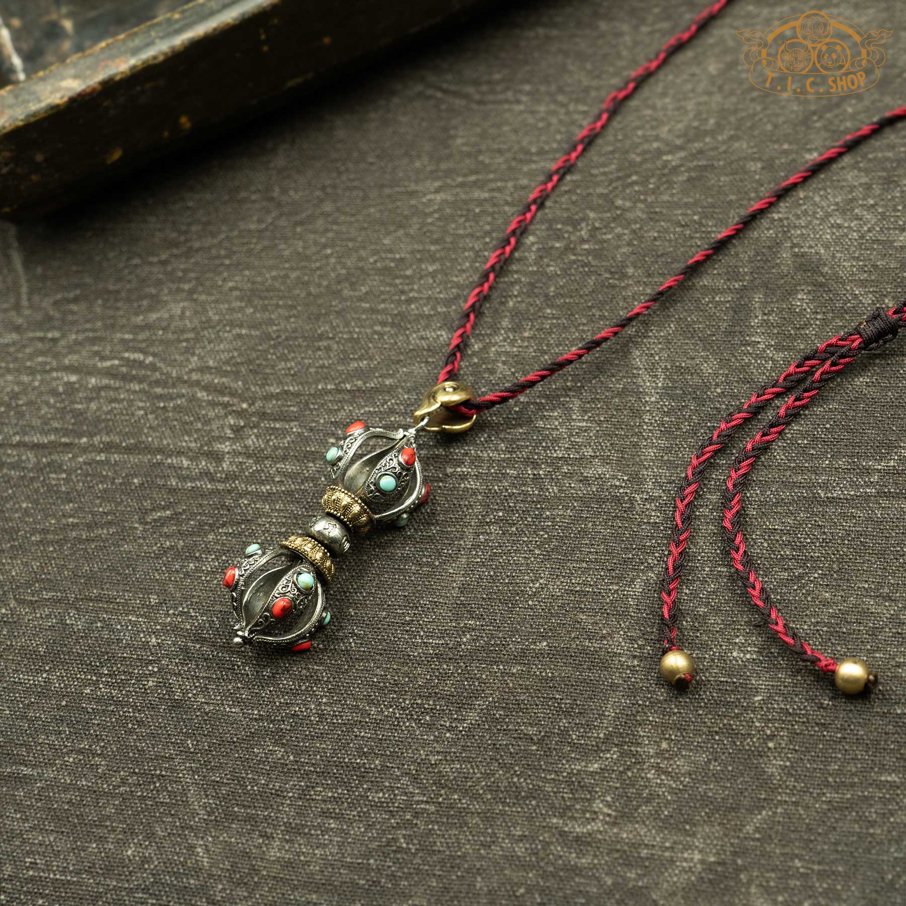 Angled view of vajra pendant with red and blue beads, showing carved design
