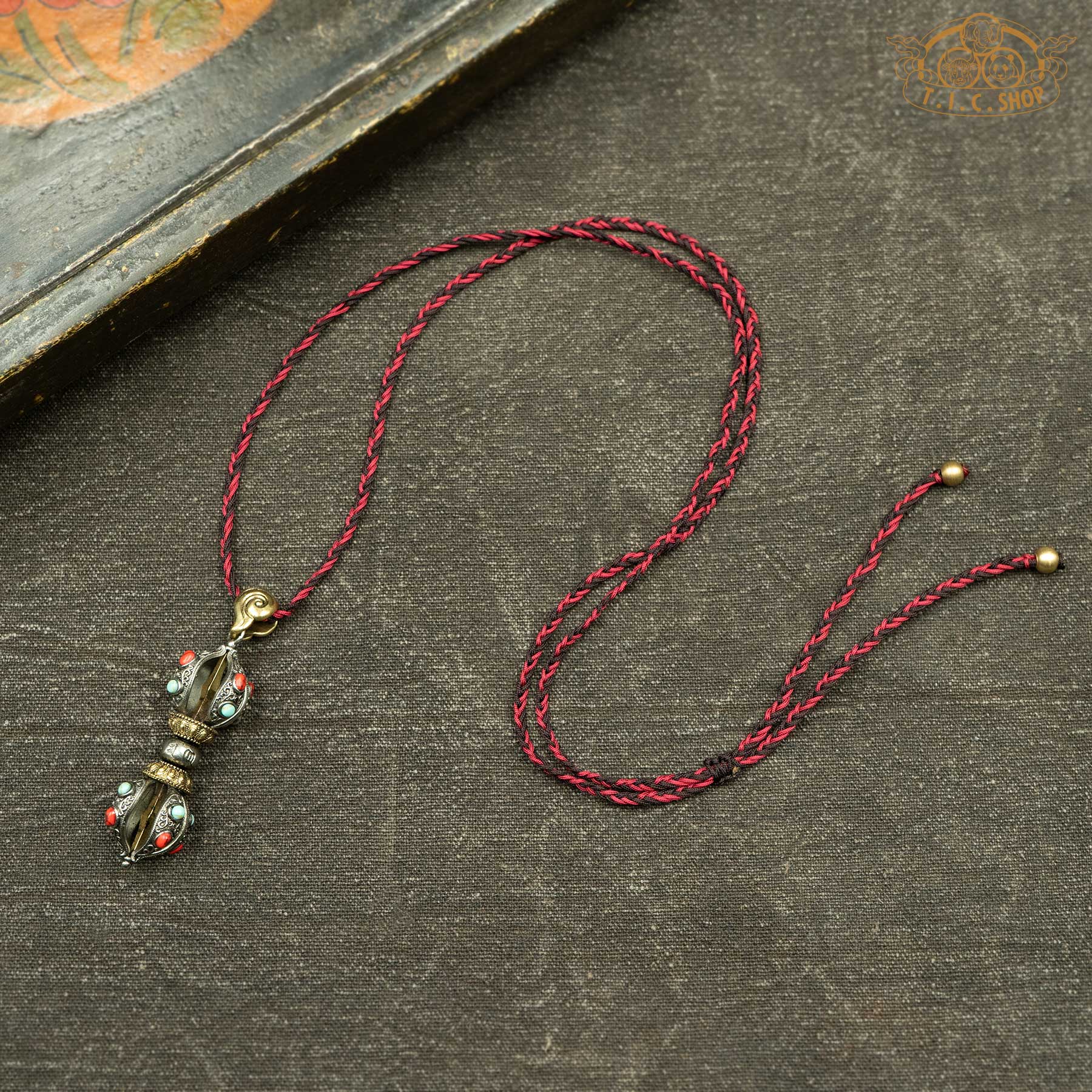 Vajra pendant with red and blue beads displayed with hand-woven red and brown rope necklace