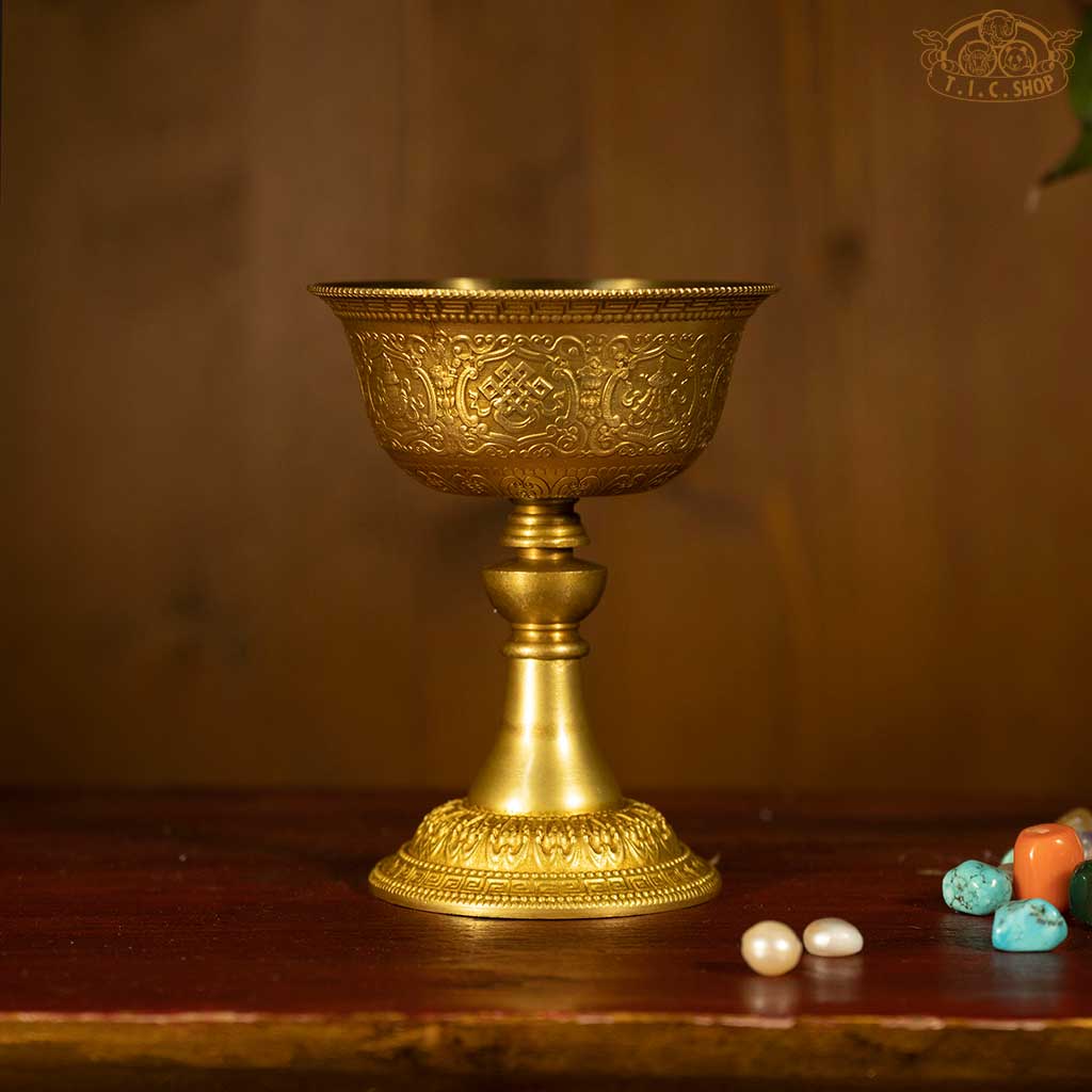 Front view of Tibetan brass butter lamp adorned with Eight Auspicious Symbols and intricate Tibetan patterns.
